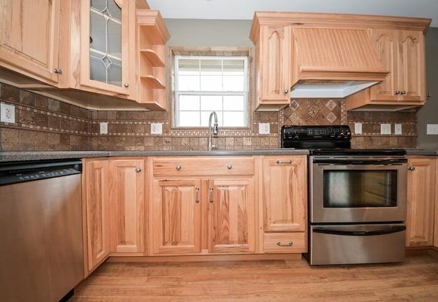 kitchen with stainless steel appliances, light brown cabinetry, custom exhaust hood, and light hardwood / wood-style flooring