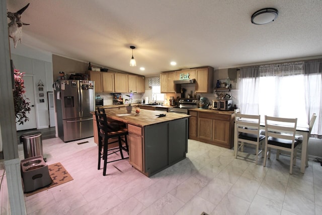 kitchen with wood counters, lofted ceiling, hanging light fixtures, a kitchen island, and stainless steel appliances