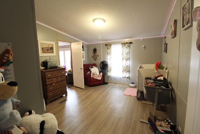 bedroom with vaulted ceiling, a textured ceiling, and light hardwood / wood-style flooring