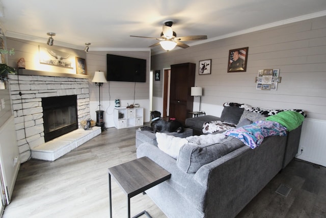 living room featuring hardwood / wood-style flooring, crown molding, a stone fireplace, and ceiling fan