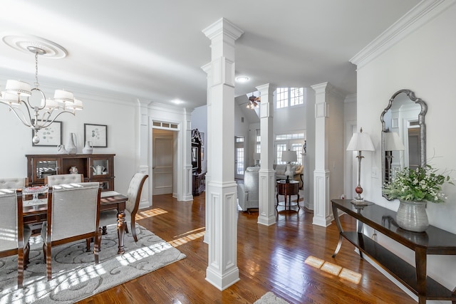 dining space with ceiling fan with notable chandelier, ornamental molding, decorative columns, and dark wood-type flooring