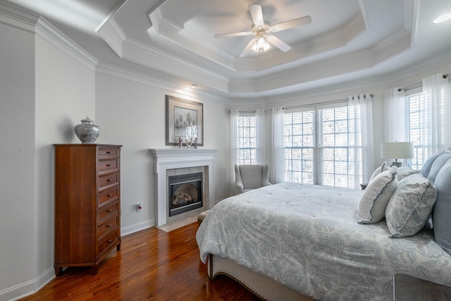 bedroom with dark hardwood / wood-style flooring, a tiled fireplace, ornamental molding, and a raised ceiling