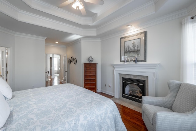 bedroom with dark hardwood / wood-style floors, a tiled fireplace, ornamental molding, ceiling fan, and a raised ceiling