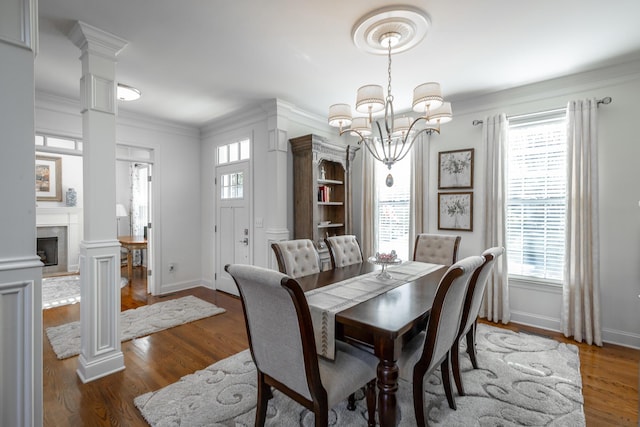 dining area featuring dark wood-type flooring, crown molding, a chandelier, and decorative columns