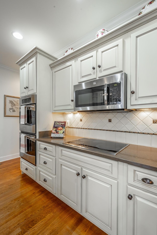 kitchen featuring appliances with stainless steel finishes, tasteful backsplash, white cabinetry, light hardwood / wood-style floors, and crown molding