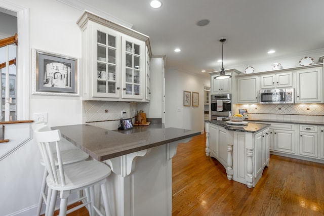 kitchen featuring appliances with stainless steel finishes, white cabinets, a kitchen bar, decorative light fixtures, and kitchen peninsula