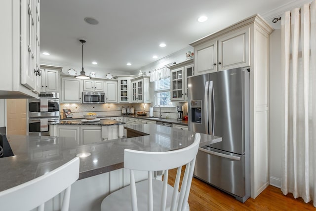 kitchen featuring sink, stainless steel appliances, wood-type flooring, decorative backsplash, and decorative light fixtures