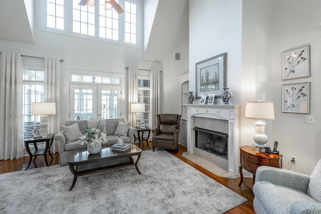 living room featuring a towering ceiling, hardwood / wood-style floors, a high end fireplace, and french doors