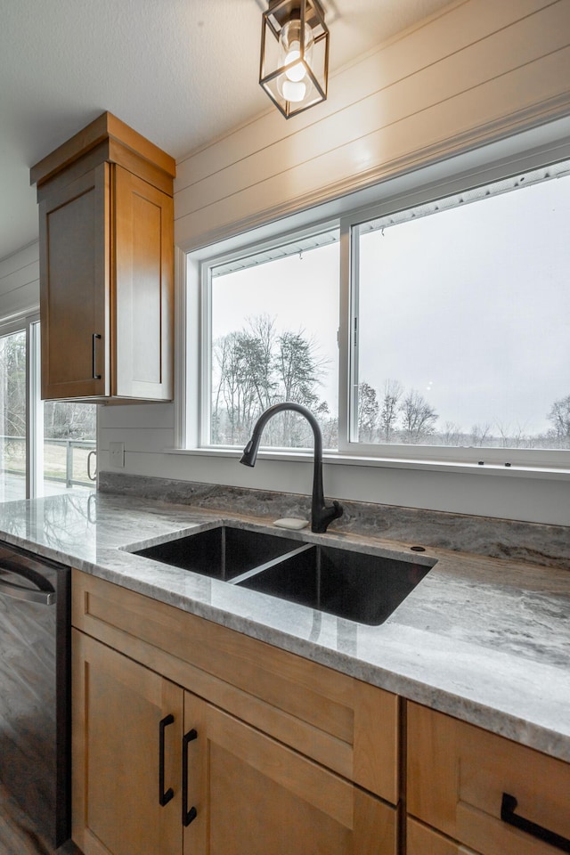 kitchen with light stone counters, sink, dishwasher, and wood walls