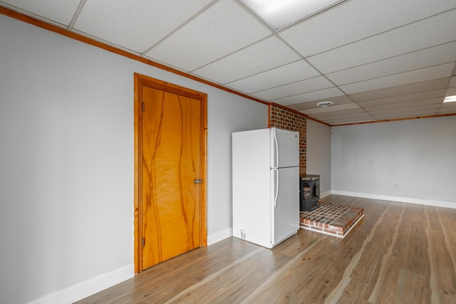 unfurnished living room with a drop ceiling, hardwood / wood-style flooring, and a wood stove