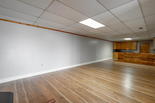 unfurnished living room featuring sink, a paneled ceiling, and light hardwood / wood-style floors