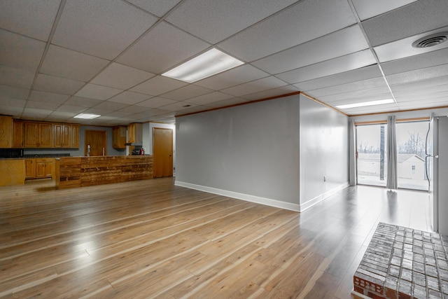 unfurnished living room featuring crown molding, a drop ceiling, and light wood-type flooring