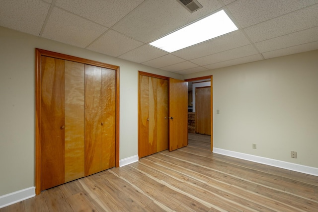 unfurnished bedroom featuring a paneled ceiling, light hardwood / wood-style floors, and two closets