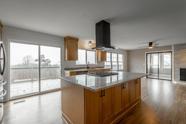 kitchen with appliances with stainless steel finishes, island range hood, sink, a center island, and light stone counters