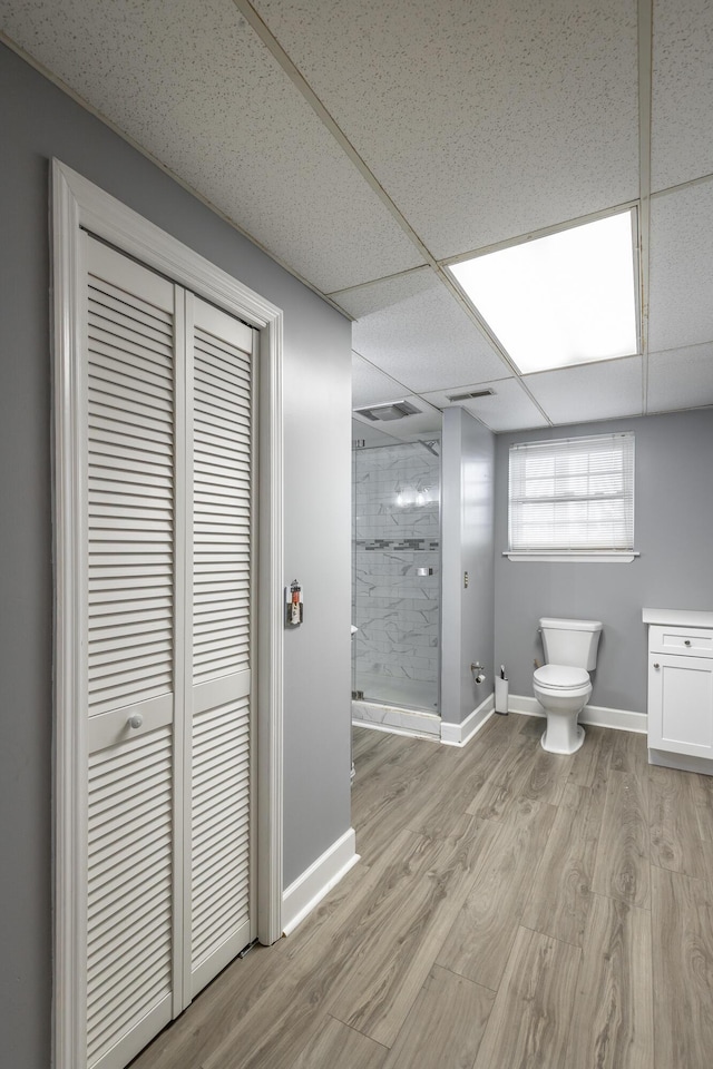 bathroom featuring vanity, wood-type flooring, a drop ceiling, a shower with shower door, and toilet