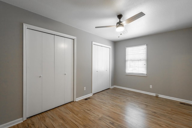 unfurnished bedroom with ceiling fan, two closets, and light wood-type flooring