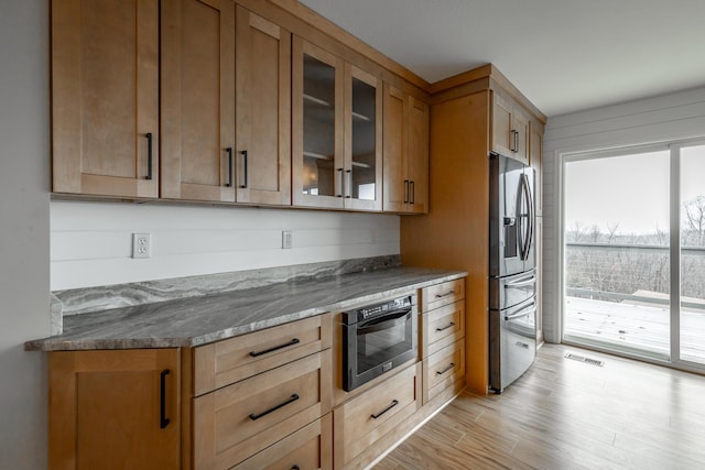 kitchen featuring light wood-type flooring, oven, light stone counters, and stainless steel fridge with ice dispenser