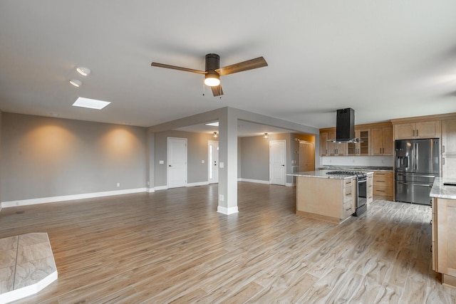 kitchen with appliances with stainless steel finishes, range hood, light stone counters, a kitchen island, and light wood-type flooring