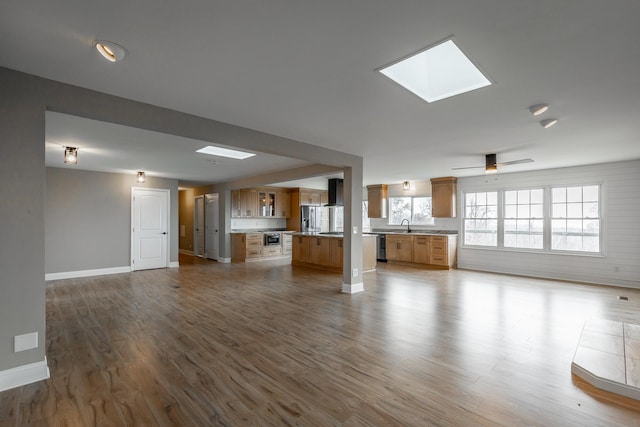 unfurnished living room featuring wood-type flooring, sink, ceiling fan, and a skylight