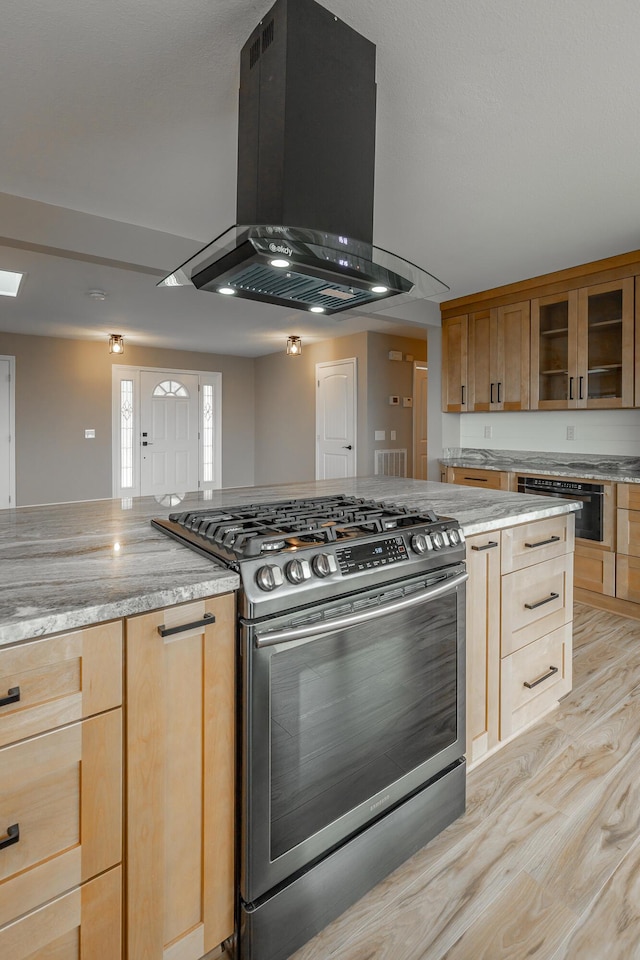 kitchen with island exhaust hood, light stone counters, light hardwood / wood-style floors, gas stove, and light brown cabinets