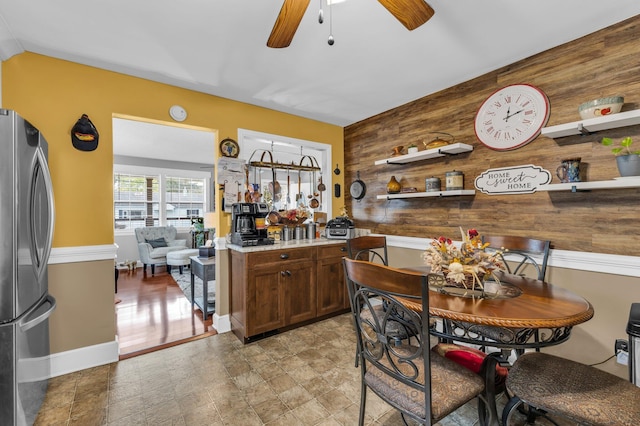 kitchen with ceiling fan, stainless steel refrigerator, and wood walls