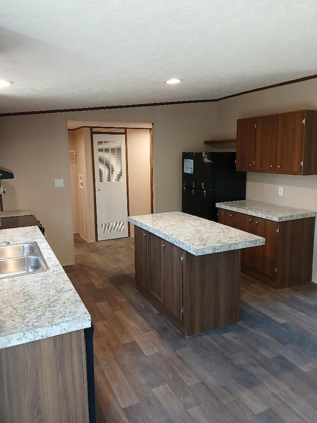 kitchen featuring dark wood-type flooring, dark brown cabinetry, sink, black refrigerator, and a kitchen island