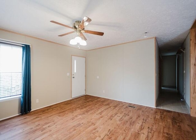 empty room with wood-type flooring, ornamental molding, ceiling fan, and plenty of natural light