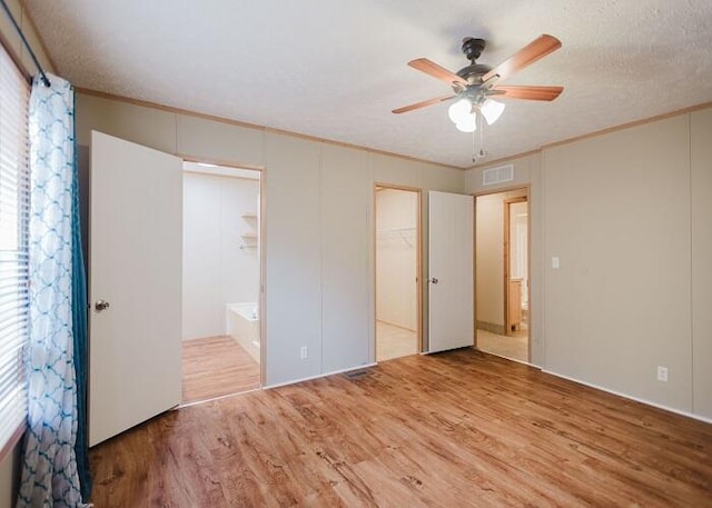 unfurnished bedroom featuring ensuite bath, a spacious closet, a closet, ceiling fan, and hardwood / wood-style floors