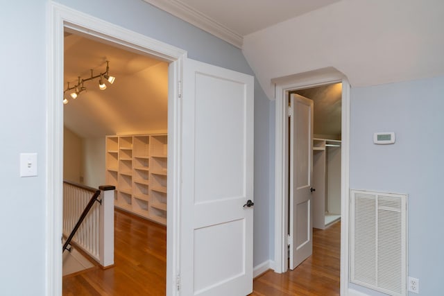 hall featuring rail lighting, lofted ceiling, ornamental molding, and light wood-type flooring