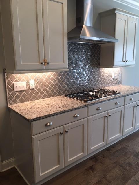 kitchen with wall chimney range hood, backsplash, light stone countertops, stainless steel gas cooktop, and white cabinets