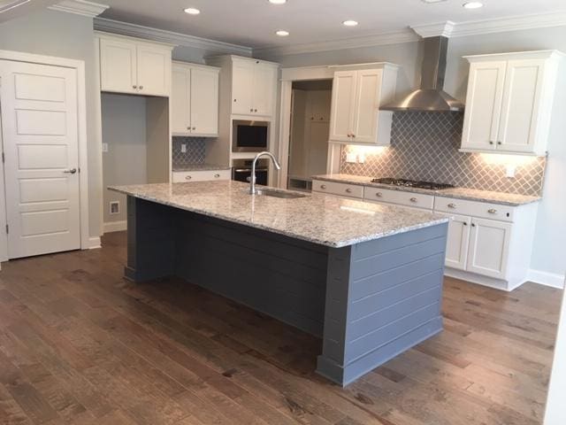 kitchen featuring wall chimney exhaust hood, sink, an island with sink, and white cabinets