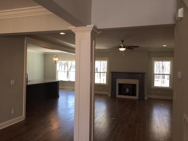 unfurnished living room with ceiling fan, ornamental molding, dark hardwood / wood-style floors, and decorative columns