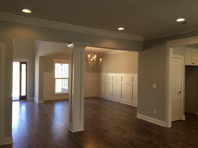 unfurnished dining area featuring crown molding, dark hardwood / wood-style flooring, a chandelier, and decorative columns