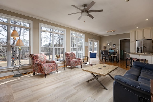 living room with crown molding, ceiling fan, and light wood-type flooring