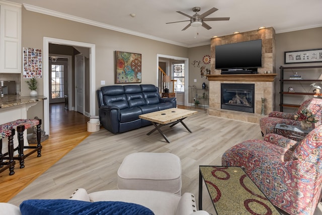 living room with ceiling fan, ornamental molding, a tile fireplace, and light hardwood / wood-style flooring