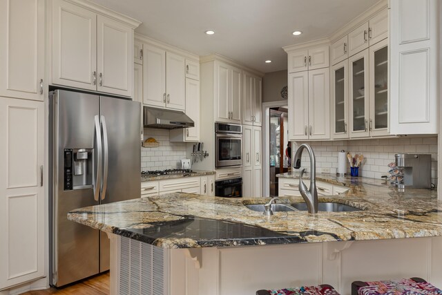 kitchen with sink, stainless steel appliances, light stone countertops, a kitchen bar, and kitchen peninsula