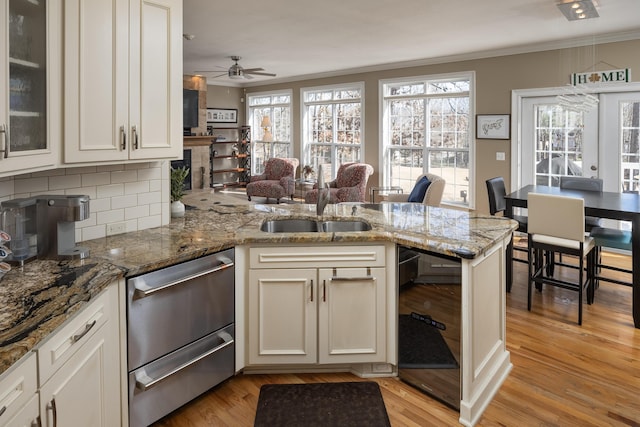 kitchen with crown molding, tasteful backsplash, light hardwood / wood-style floors, stone countertops, and kitchen peninsula