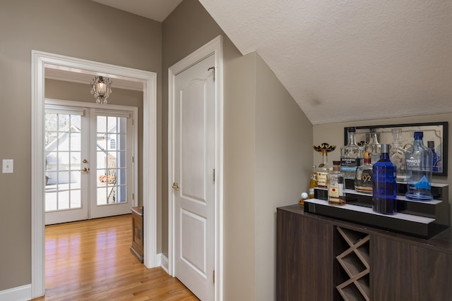 bar featuring dark brown cabinetry, a textured ceiling, light wood-type flooring, and french doors