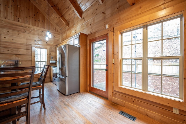 dining area with light wood-type flooring, wooden ceiling, lofted ceiling with beams, and wood walls