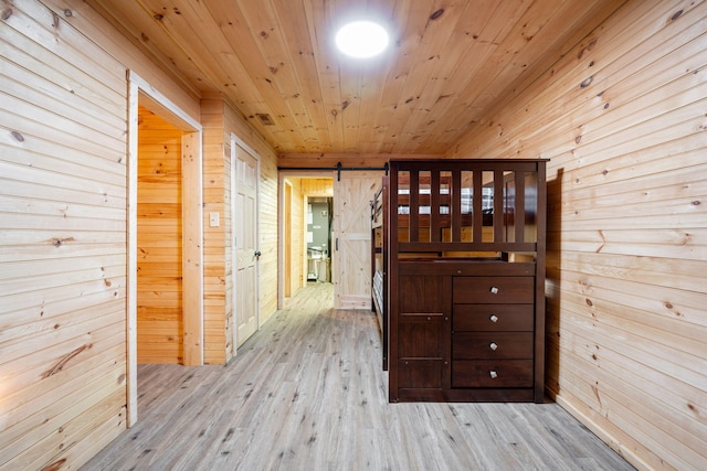 hallway with a barn door, wooden walls, wooden ceiling, and light wood-type flooring