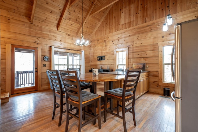 dining room featuring light wood-type flooring, a wealth of natural light, wood ceiling, and wooden walls