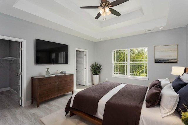 bedroom with a walk in closet, a raised ceiling, a closet, ceiling fan, and light hardwood / wood-style floors