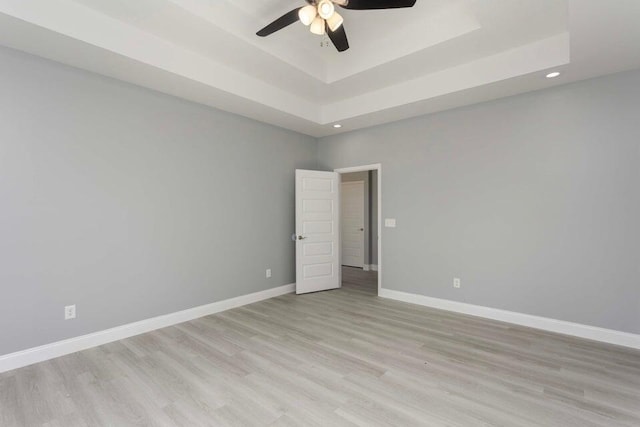 empty room with ceiling fan, a raised ceiling, and light hardwood / wood-style flooring