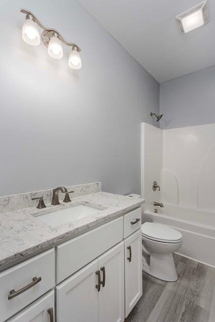 full bathroom featuring vanity, wood-type flooring, washtub / shower combination, and toilet