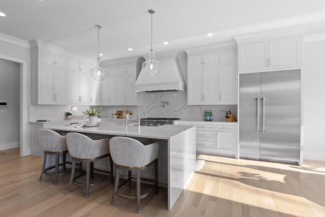 kitchen featuring a kitchen bar, a center island with sink, premium range hood, and built in refrigerator