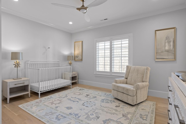 bedroom featuring a crib, ornamental molding, and light hardwood / wood-style floors