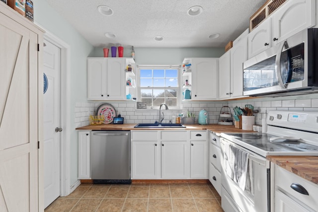 kitchen with appliances with stainless steel finishes, sink, butcher block countertops, and white cabinets