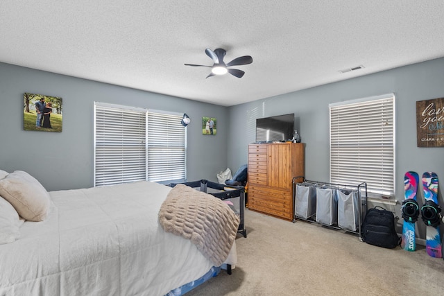 bedroom with ceiling fan, light colored carpet, and a textured ceiling