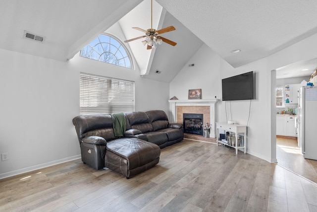 living room with a tile fireplace, high vaulted ceiling, ceiling fan, and light wood-type flooring