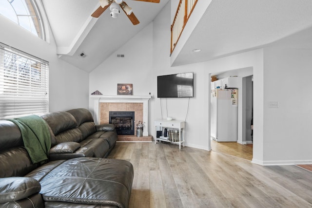 living room featuring a tiled fireplace, high vaulted ceiling, and light hardwood / wood-style floors